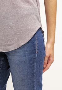 Grå topp med kort ärm och rundad nederkant, tillsammans med blå jeans i slim fit med subtil sömdetalj vid fickan.