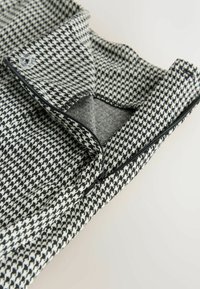 Čierne a biele tkaniny s houndstooth vzorom, s prehnutým golierom, obsahujúce čierny zips a kontrastnú podšívku.