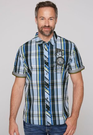 Short-sleeve plaid shirt in blue, green, and black; features buttons, a collar, logo patch, and contrasting trim on sleeves.