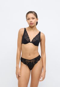 Zwarte kanten lingerie set met een diep uitgesneden bh met geschulpte randen en bijpassende doorschijnende string met bloemenmotief. Soepele textuur en verfijnd ontwerp.