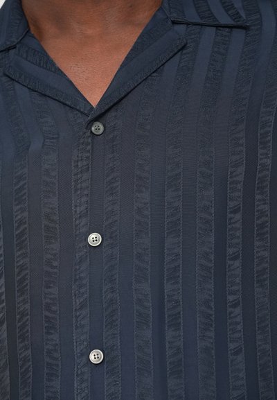 Knapp-up skjorta i mörk marinblå med vertikala strukturerade ränder, två knappstängningar, mjukt tyg och en notchad kragsdesign.
