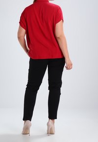 Chemise rouge à manches courtes, tissu lisse, détail de col, assortie à un pantalon noir slim-fit et des chaussures à talons beiges.