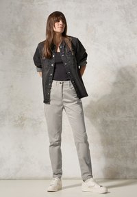 Giubbotto di jeans neri sopra una maglietta nera, abbinato a pantaloni grigio chiaro e sneakers bianche. L'outfit presenta dettagli con bottoni e una vestibilità dritta.