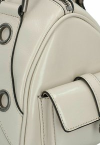 Borsa in finta pelle color crema con forma arrotondata, accentata in nero, dotata di accessori in metallo e chiusura con zip. Presenta una piccola tasca frontale.
