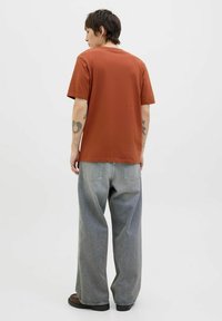 Rustfarvet bomulds T-shirt med korte ærmer, kombineret med løstsiddende lys grå denimjeans. Minimalistisk design uden synlige mønstre.