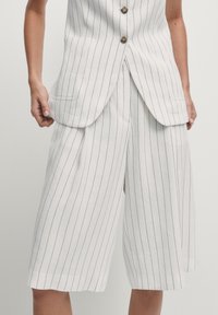 Witte, gestreepte culottes met een losse pasvorm, voorzien van zijzakken en een wijde pijpdesign. De stof lijkt lichtgewicht met een strakke textuur.