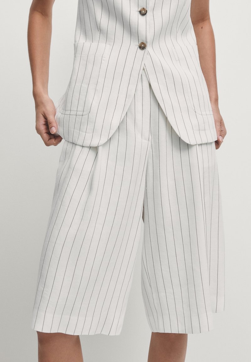Witte, gestreepte culottes met een losse pasvorm, voorzien van zijzakken en een wijde pijpdesign. De stof lijkt lichtgewicht met een strakke textuur.