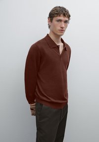 Maglione polo a maniche lunghe color amaranto realizzato in tessuto morbido, con colletto classico e patta con tre bottoni. Abbinato a pantaloni scuri.