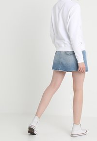 Vit crew-neck sweatshirt i kombination med en blå denim minikjol. Kjolen har en fransad fåll och outfiten kompletteras med vita högenskor.