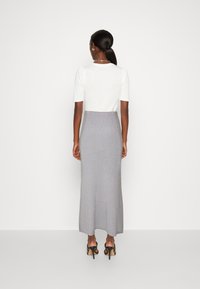 Top blanco de manga corta combinado con una falda maxi gris, ajustada al cuerpo. La modelo lleva sandalias de tacón negro. Diseño simple, textura de punto.