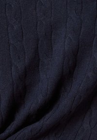 Marinefarbene Kabelstrickpullover aus Stoff mit weicher Textur, der erhöhte, gedrehte Muster auf der Oberfläche in einem glatten Finish aufweist.