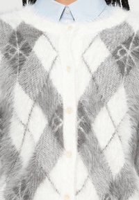 Szürke és fehér argyle mintás kardigán puha, bolyhos anyagból, gombos elülső résszel, gyöngyszerű gombokkal, alatta világoskék galléros inggel.