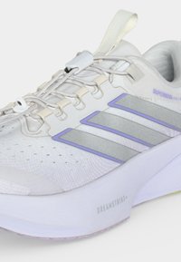 Λευκό αθλητικό παπούτσι Adidas με ανοιχτό μοβ ρίγες, ελαστικά κορδόνια χωρίς δέσιμο, μαλακή σόλα με ετικέτα "DREAMSTRIKE+" και κείμενο "SUPERNOVA".