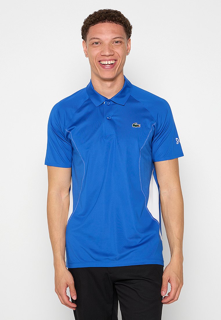 Polo shirt bleu à manches courtes, avec un tissu texturé, un col à deux boutons et des accents blancs sur les côtés. Logo sur le côté gauche de la poitrine.