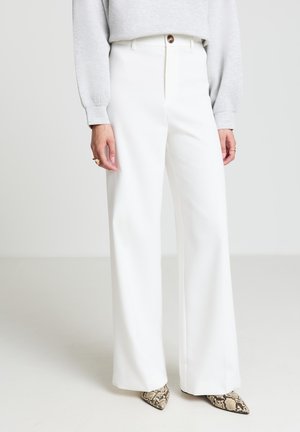 Pantalon blanc à jambes larges avec une texture lisse, doté d'une fermeture à boutons sur le devant et d'une taille haute, assorti à un sweat-shirt gris clair.