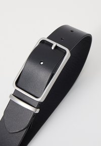 Cinturón de cuero negro con una textura suave, que cuenta con una hebilla rectangular plateada y un ojal de metal, diseñado con agujeros espaciados uniformemente.