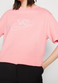 Růžové bavlněné tričko s krátkými rukávy, zdobené bílým vyšívaným logem Nike na hrudi a s uvolněným, boxy střihem.