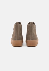 Bottines en cuir suédé marron avec une semelle en caoutchouc texturée, des panneaux latéraux élastiques et une languette arrière pour un accès facile. Présentent des accents métalliques minimaux.