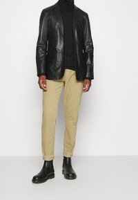 Svart skinnblazer över en svart polotröja, kombinerad med beige kortade byxor och svarta ankelboots. Mjuk textur, skräddarsydd passform.