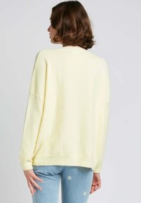 Un pull surdimensionné jaune clair avec une texture douce, des épaules tombantes et un ourlet côtelé, associé à un jean bleu avec des broderies florales.