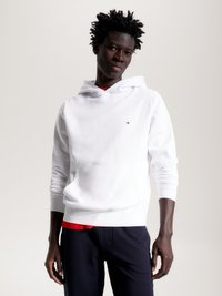 Sweatshirt branco com bolso canguru e punhos canelados, sobre uma camisa vermelha, combinado com calças escuras. Apresenta um logo no peito.