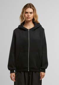 Mustahi zip-up hoodie musta, ulko-ovessa vetoketju, isot etupussit ja pieni sydänlogo rinnassa. Pehmeä rakenne ja rento istuvuus.