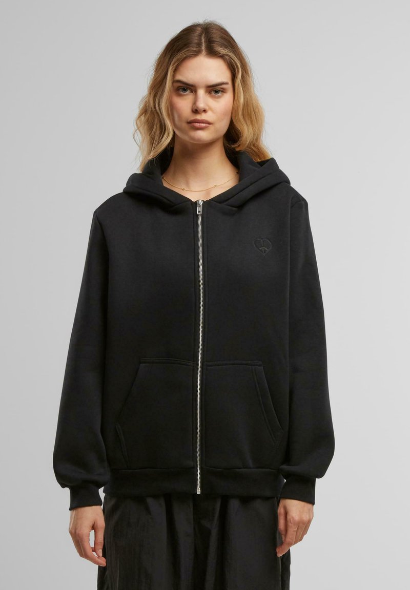 Mustahi zip-up hoodie musta, ulko-ovessa vetoketju, isot etupussit ja pieni sydänlogo rinnassa. Pehmeä rakenne ja rento istuvuus.