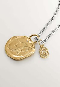 Colgante dorado en una cadena de plata, que presenta un medallón ovalado texturizado y un charm más pequeño con la letra "G" adornada.