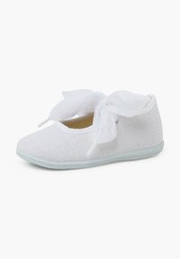 Bailarina de tela blanca con upper de malla texturada, punta redondeada y dos lazos de cinta blanca transparente atados en la parte delantera. Suela suave.