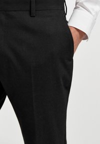 Schwarze maßgeschneiderte Hose aus strukturiertem Stoff, mit slim fit und Seitentaschen. Der Bund hat ein einfaches, sauberes Finish.