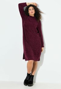 Abito a maglia di un profondo bordeaux con maniche lunghe, collo alto, spacchi laterali e una texture morbida; abbinato a stivali neri con lacci alla caviglia.