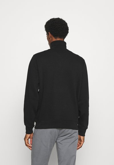 Sweatshirt noir à col montant avec manches longues, coupe décontractée, et poignets et ourlet côtelés. Texture de tissu lisse, design minimaliste, sans motifs.