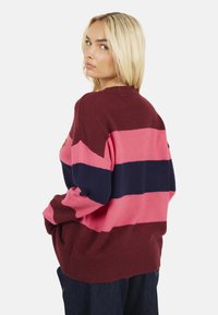 Maglione oversize a righe bordeaux, rosa e blu navy. Morbido maglione a coste con maniche lunghe e scollo rotondo, caratterizzato da un logo discreto.