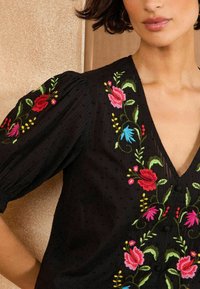 Fekete bl�úz élénk virágmintákkal rózsaszín, piros és kék színben. Texturált anyag, V-nyakkivágással és puffos rövid ujjal.