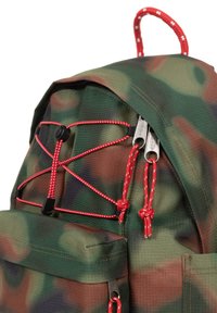 Zaino camouflage con tessuto testurizzato, dettaglio in corda elastica rossa, doppie cerniere metalliche e una maniglia superiore per il trasporto.