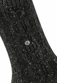 Calzino nero lavorato a maglia con motivo testurizzato e macchie bianche. Presenta un accento metallico rotondo con logo vicino alla parte superiore. Materiale morbido in mistura di lana.