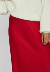 Jupe en satin rouge avec une texture lisse, dotée d'une taille haute. Un pull en laine blanche duveteux avec des détails texturés est porté par-dessus.