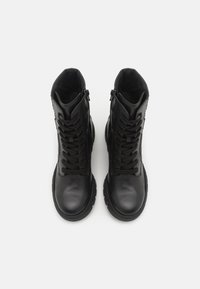 Botas de cuero negras hasta el tobillo con punta redonda, cordones largos, cremallera lateral y acentos texturizados. Acabado suave y suela acolchada.