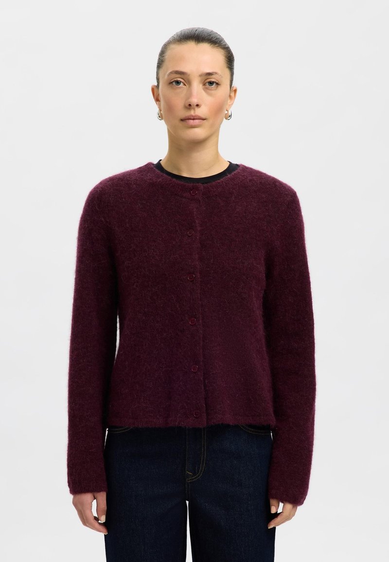 Vinröd kofta tillverkad av mjukt, luddigt material. Har en rund halsringning, långa ärmar och knappstängning fram.