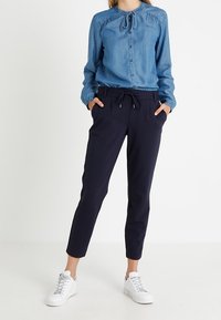 Denim-tupakuvattu paita, jossa on kiristettävä kaula, yhdistettynä merimiessinisiin kapeneviin housuihin ja valkoisiin tennareihin. Sujuva kangas ja istuva malli.