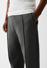 Pantalon gris en tissu doux, avec une coupe décontractée, des poches latérales et des détails de couture discrets le long des coutures avant.