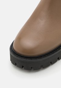 Bruine leren enkelboot met een ronde neus, een gestructureerd oppervlak en een dikke zwarte rubberen zool met een gekarteld patroon.
