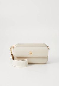 Beige Lederhandtasche mit goldenem Logo, ausgestattet mit einem Reißverschluss und einem abnehmbaren weißen Riemen. Glatte Textur und rechteckige Form.