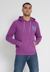 Violet huppari, jossa on etutasku, ja rintaan on painettu sininen kuvioitu logo. Vaaleansiniset kiristysnauhat. Pehmeä pinta.