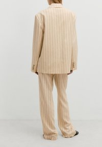 Beige gestreepte pakset met een loose-fit blazer en wijde broek, gemaakt van textuurstof met knopen details op de mouwen.