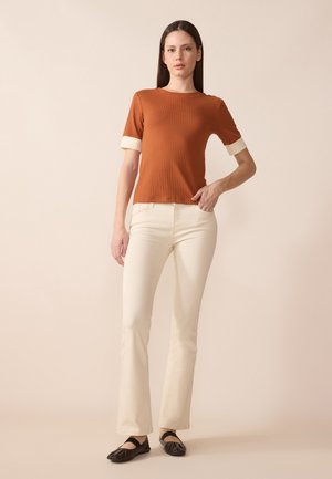 Haut court à rayures marron avec des accents crème, associé à un pantalon évasé crème et des chaussures plates noires. Texture lisse et design ajusté.