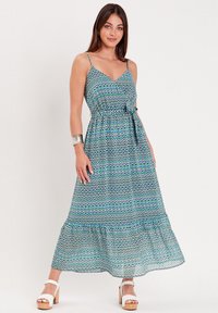 Robe maxi à motif géométrique bleu et vert, avec un décolleté en V, des bretelles ajustables, une taille nouée et une jupe à volants.