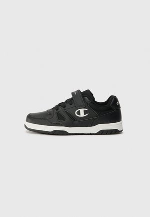 Chaussure de sport noire avec une tige en mesh et en synthétique, accents blancs, sangle ajustable et semelle en caoutchouc pour l'adhérence.
