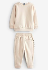 Beige sweatshirt og matchende joggers lavet af blødt stof. Sweatshirten har ribbede manchetter; joggersne har et sideprint og elastisk talje.