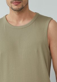Khaki ärmelloses, geripptes Tanktop mit rundem Ausschnitt, das eine weiche Textur und dezente Nähte an den Kanten aufweist.
